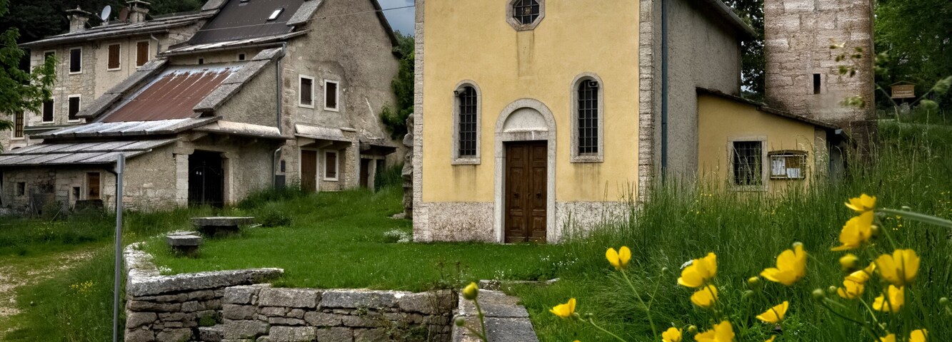 Una iglesia con un campanario, rodeada de casas de piedra y muros amarillos.