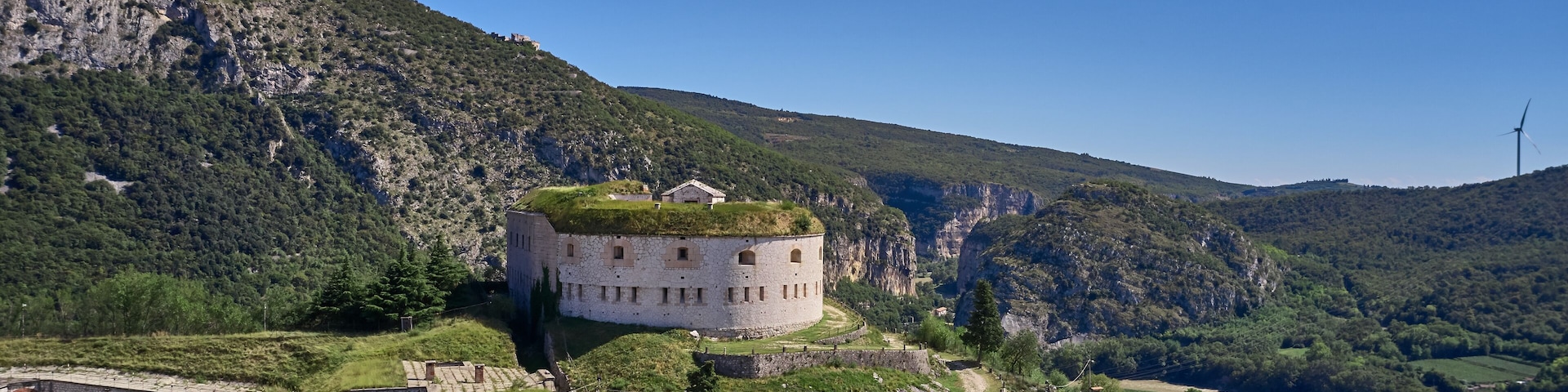 Un castillo histórico en una colina con vistas a un río, rodeado de exuberante vegetación y montañas.