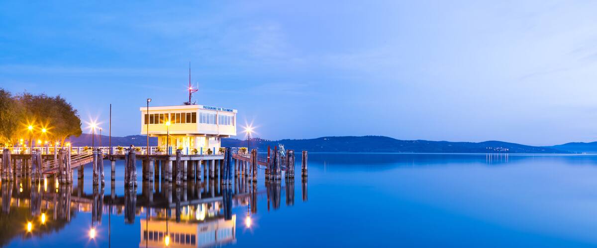 A waterfront building with a dock extending into calm water, surrounded by hills.