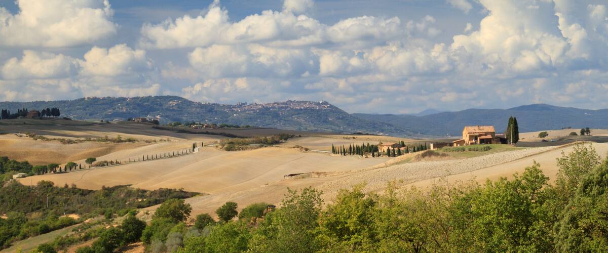 Rolling hills, a distant mountain range, and a small building with a red roof.