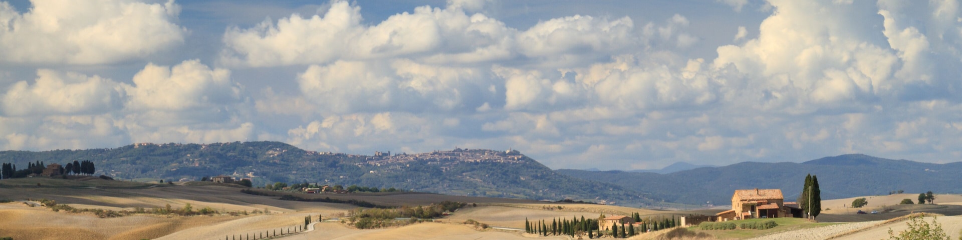 Rolling hills, a distant mountain range, and a small building with a red roof.