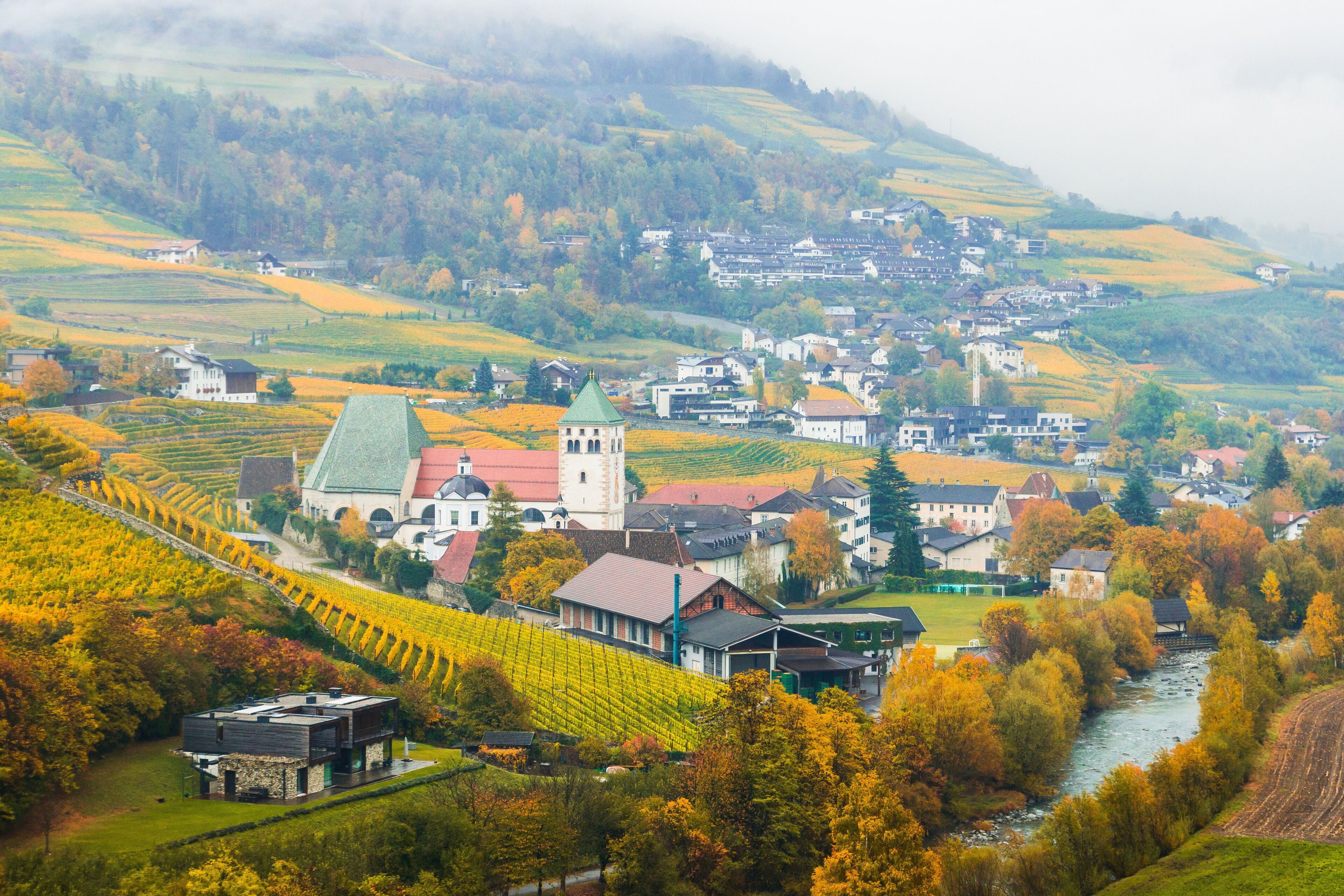 Picturesque autumnal view on Novacella, Varna, Bolzano in South Tyrol. Mountain scenery in Northern Italy. View from the top on the mountain valley. Colourful vineyards and yellow foliage on trees.