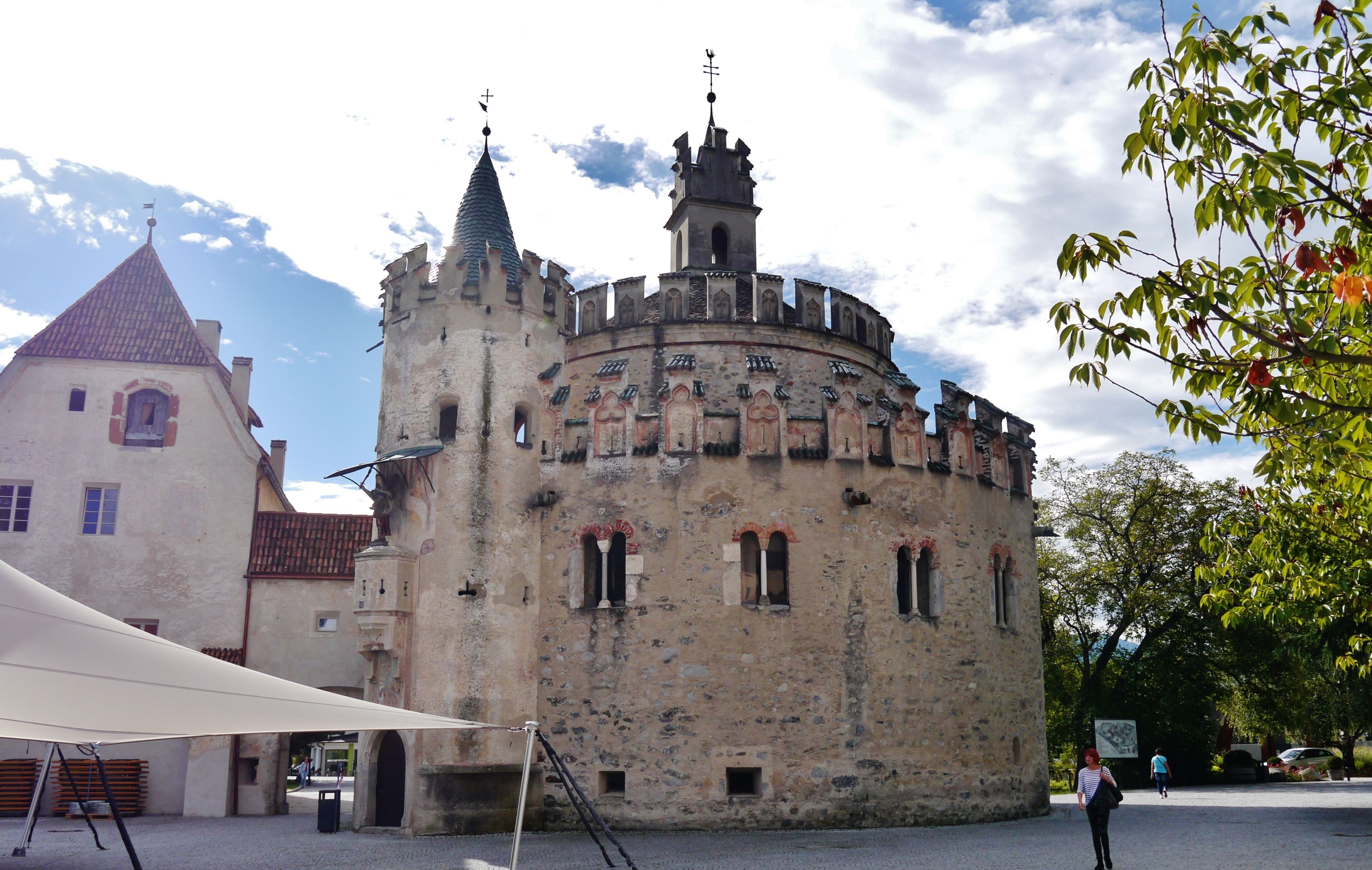 A historic castle with a round tower and a smaller building with a red roof.
