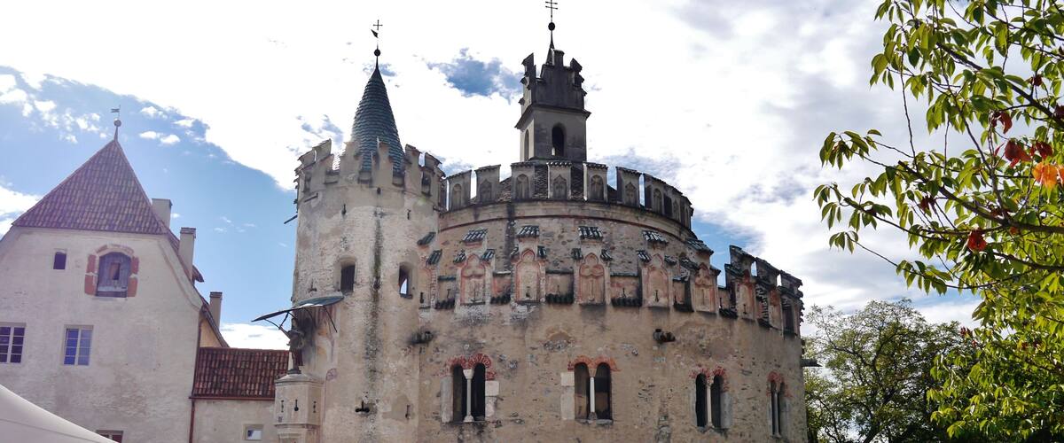 A historic castle with a round tower and a smaller building with a red roof.