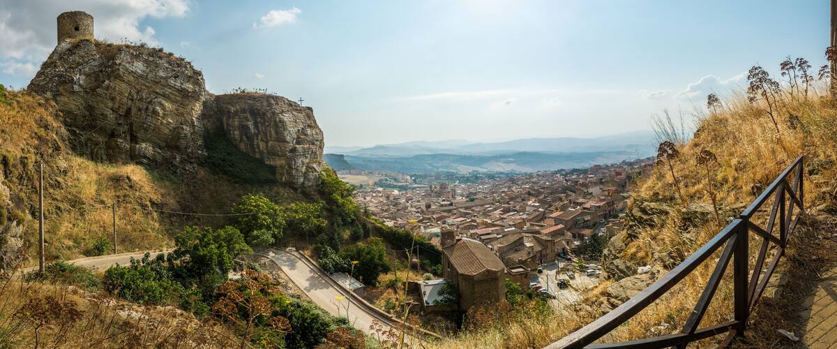 A town nestled in a valley with a prominent rock formation and a cross on top.