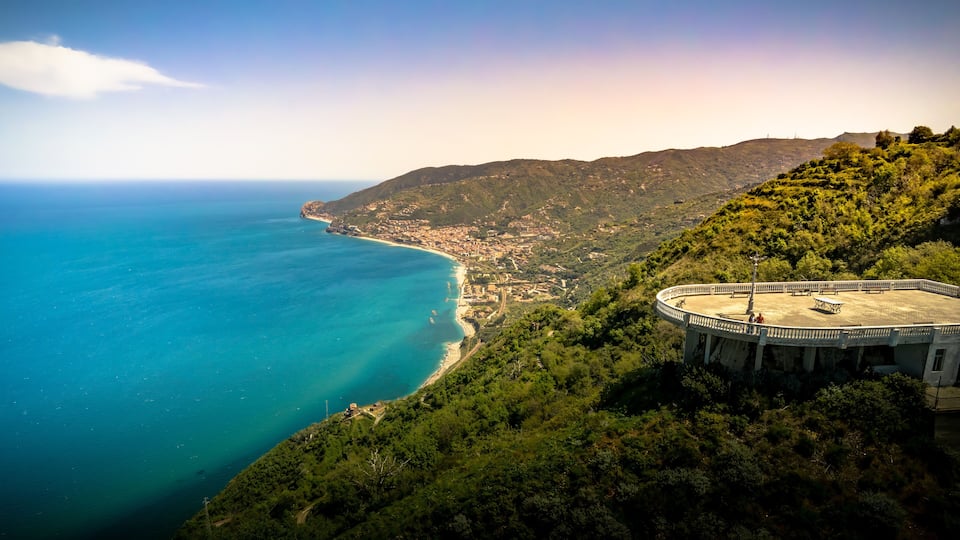 A coastal landscape with a circular viewing platform overlooking a beach and the sea.