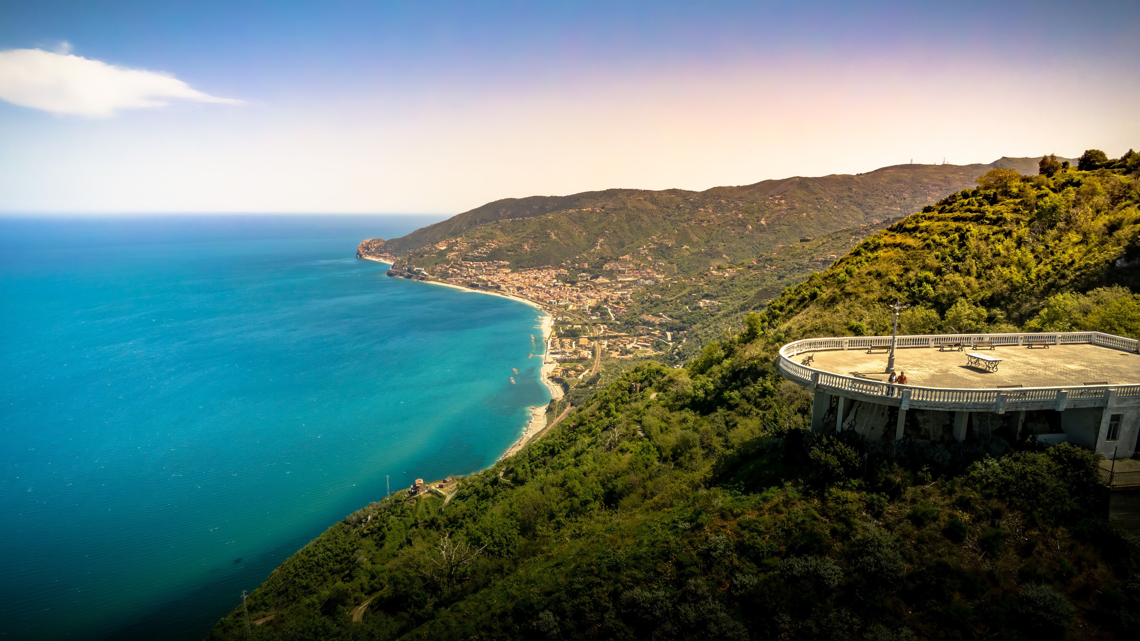A coastal landscape with a circular viewing platform overlooking a beach and the sea.