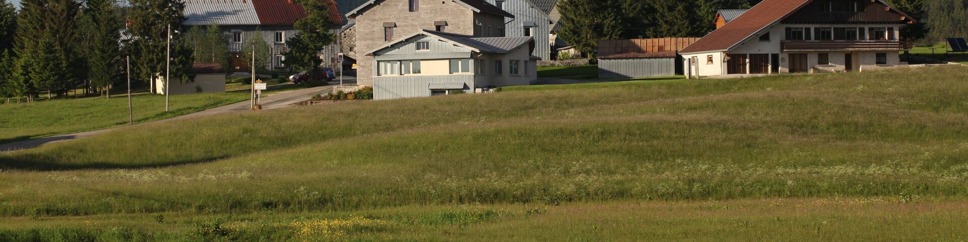 A rural landscape with a church, residential buildings, and a forested hill in the background.