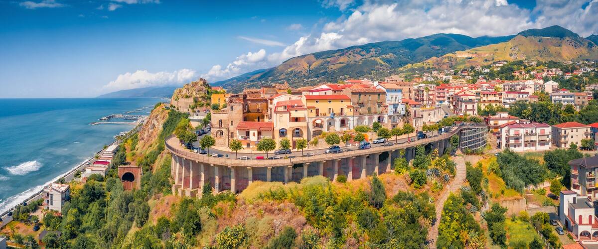 A coastal town with colorful buildings, a bridge, and a mountainous backdrop.