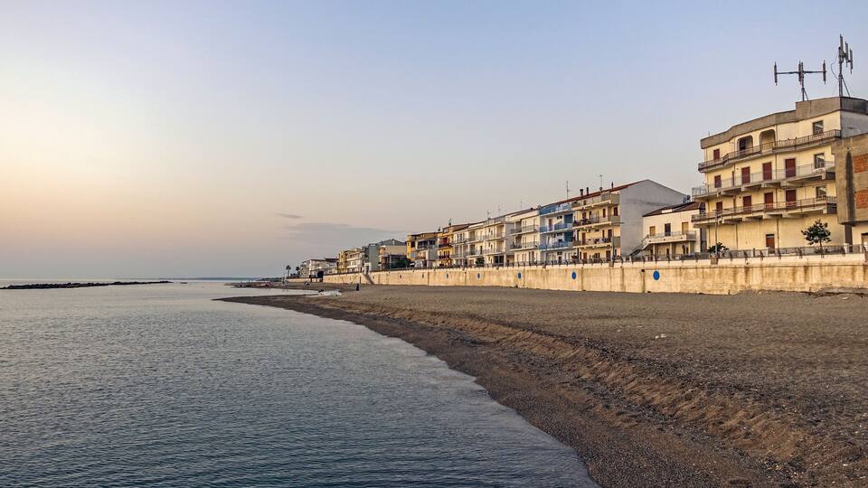 A coastal promenade with buildings along the shore and a calm sea.
