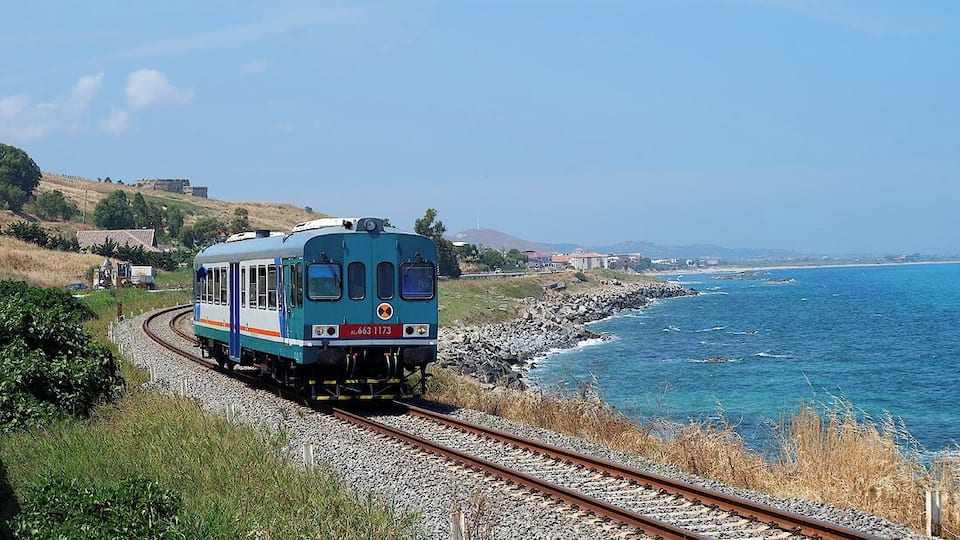 A train on tracks near a coastal area with a clear sky.