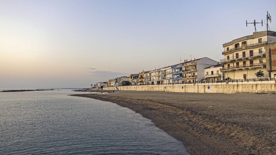 A coastal town with a sandy beach, multi-story buildings, and a clear sky.