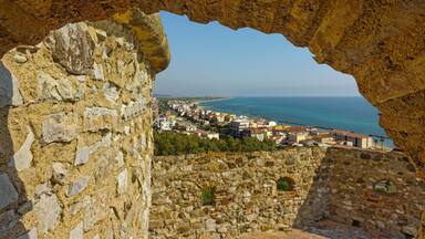 A coastal town viewed through an ancient stone archway.