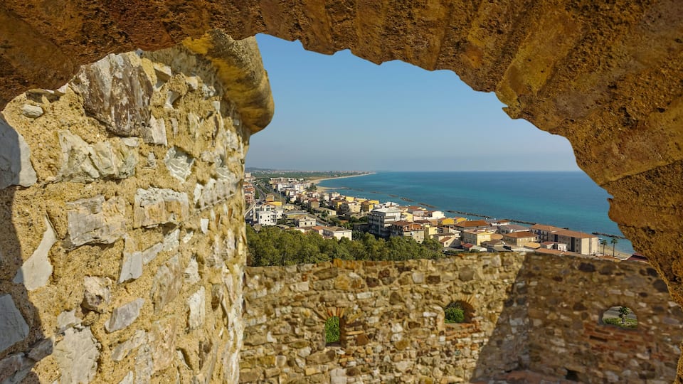 A coastal town viewed through an ancient stone archway.