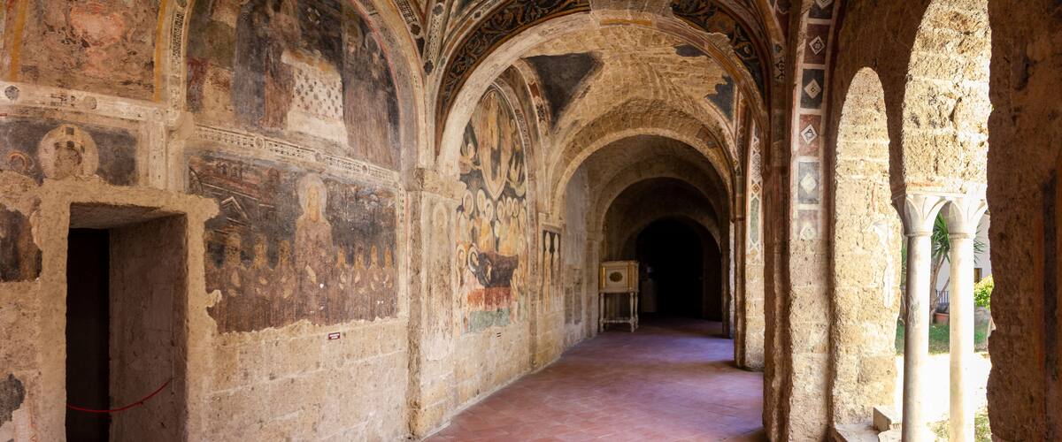 An ancient corridor with arched ceilings and detailed frescoes.