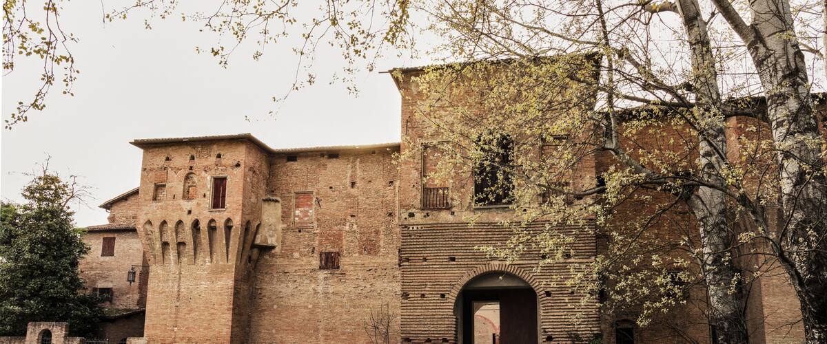 A historic brick building with arched doorways and a gravel courtyard.