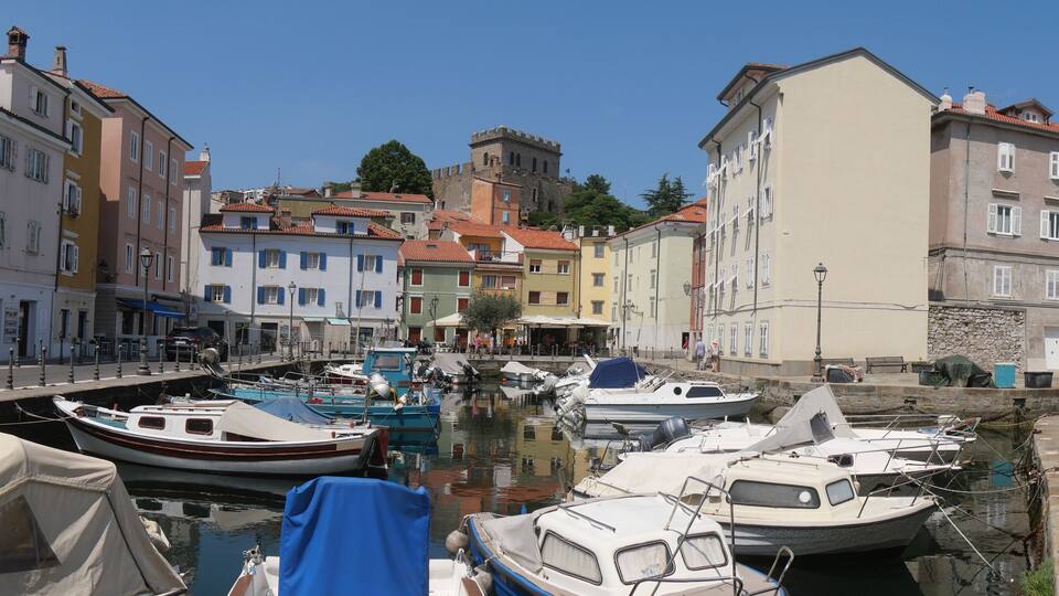 A marina with boats docked, surrounded by colorful buildings and a castle in the background.