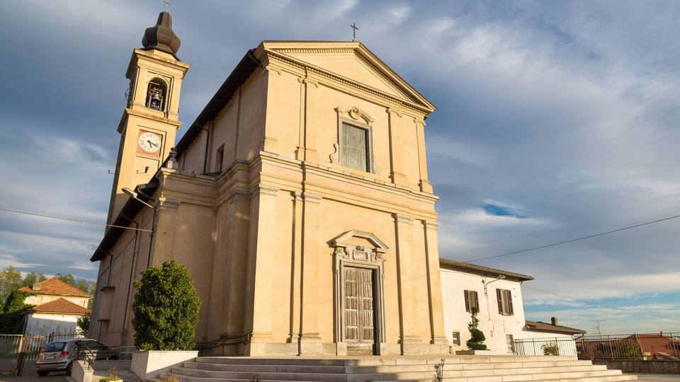 A beige church with a bell tower and a clock, surrounded by steps and potted plants.