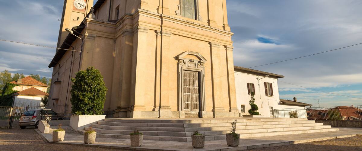 A beige church with a bell tower and a clock, surrounded by steps and potted plants.