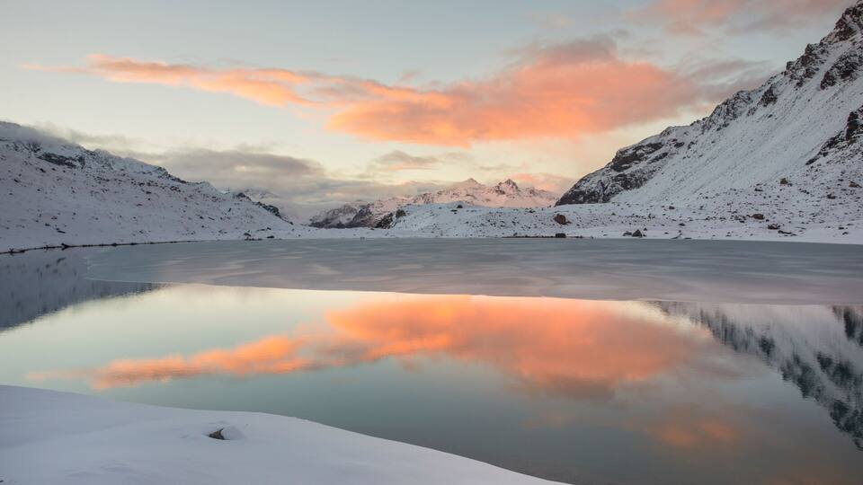 A snow-covered mountain range with a frozen lake reflecting the sky.