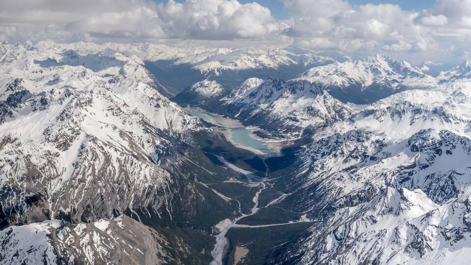 A snow-covered mountain range with a glacial valley and a lake.