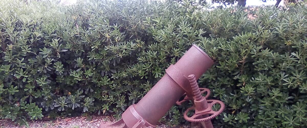 A rusted metal structure with gears, surrounded by a hedge.