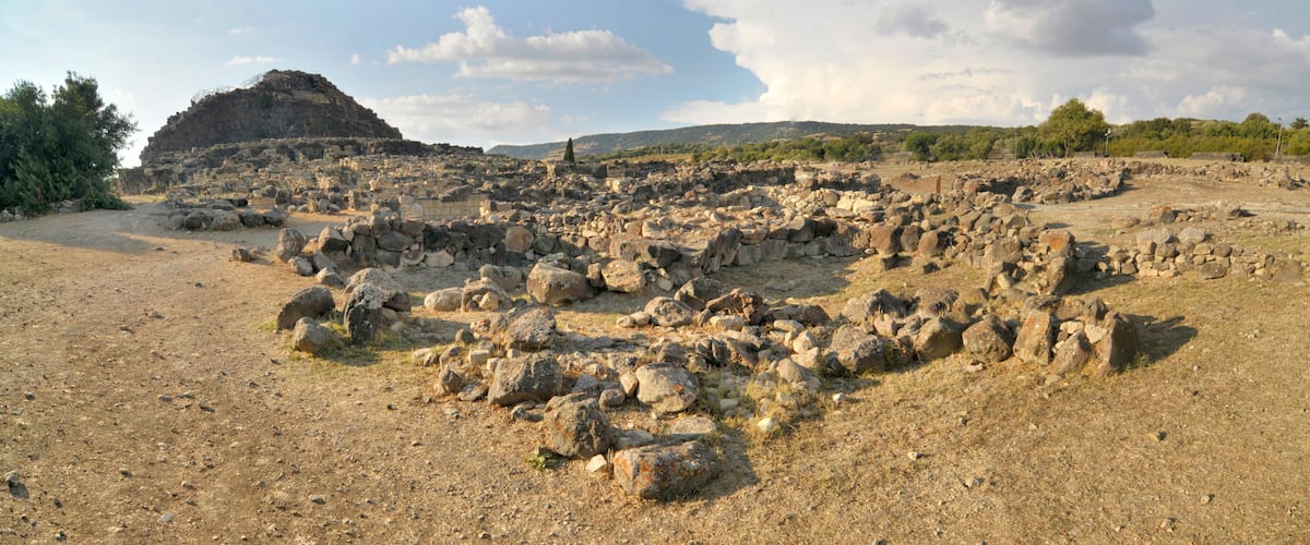 An ancient ruin with scattered stones and a large rock formation in the background.
