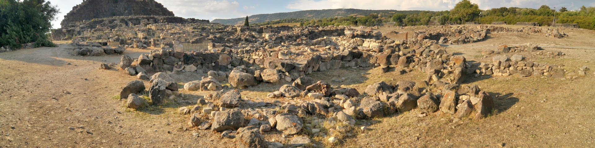 An ancient ruin with scattered stones and a large rock formation in the background.