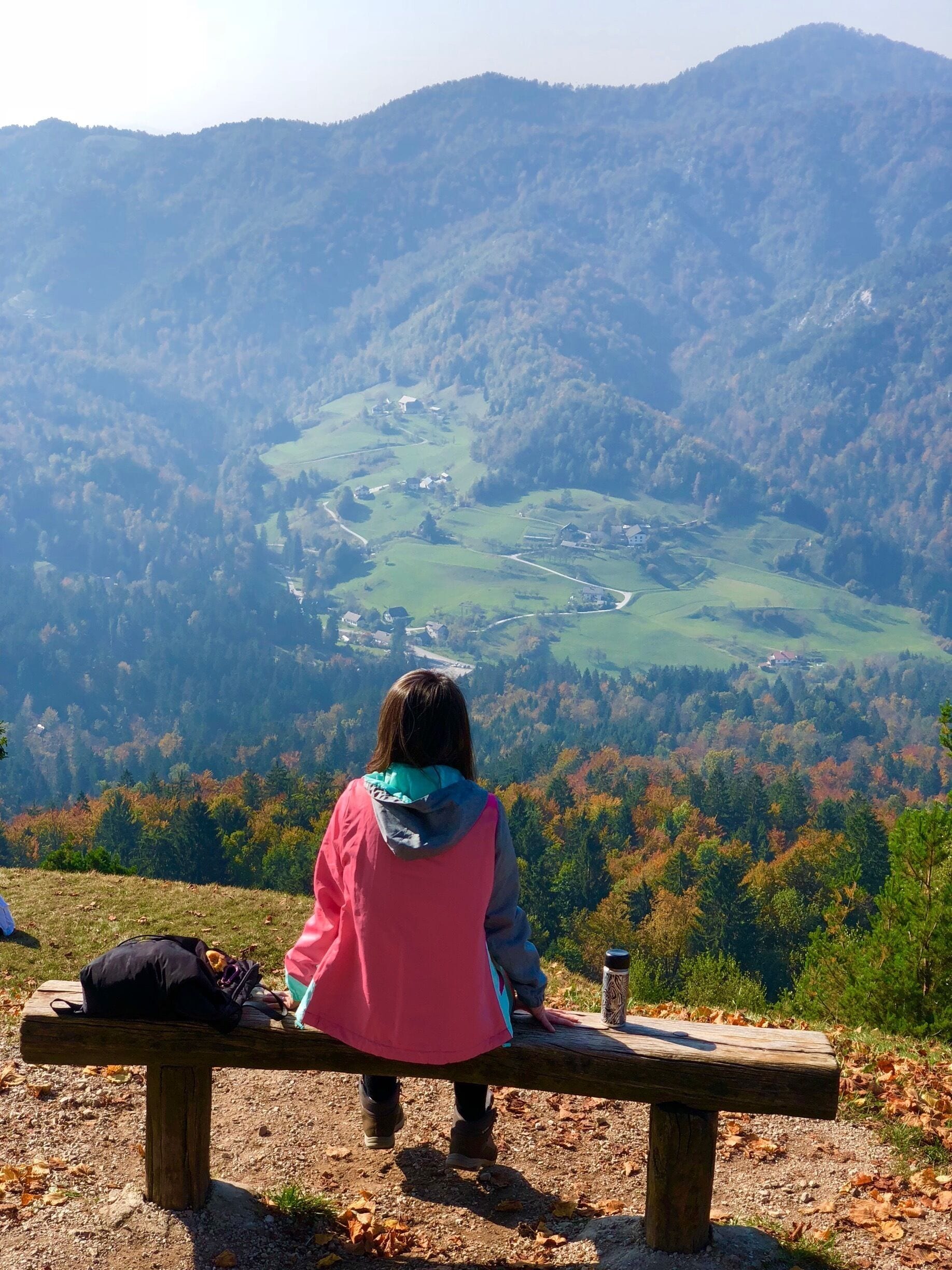 A person sitting on a bench overlooking a valley with a lake and houses.