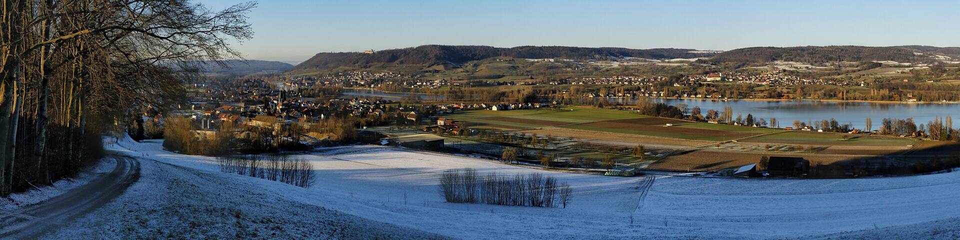 A snow-covered landscape with a river, a town, and a hilly backdrop.