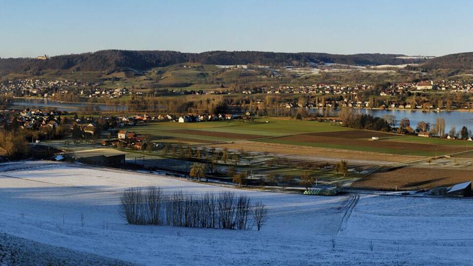 A snow-covered landscape with a river, a town, and a hilly backdrop.