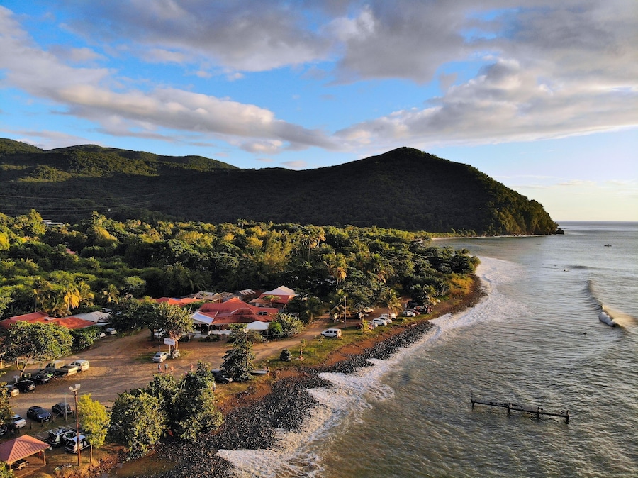 Guadeloupe beach drone sunset view. Plage Caraibe black beach aerial view in Pointe Noire. Backlit ocean wave shadows.