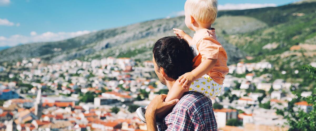 A man holding a child with a view of a densely packed town and hills in the background.
