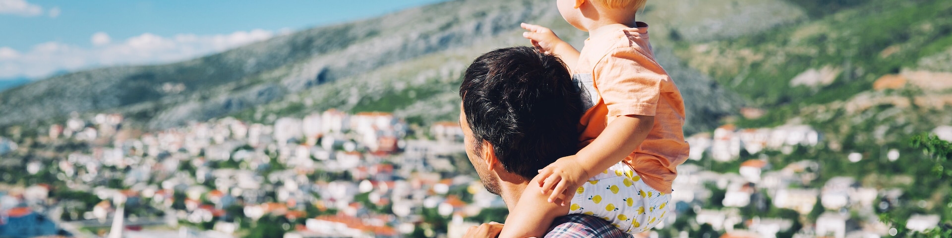 A man holding a child with a view of a densely packed town and hills in the background.