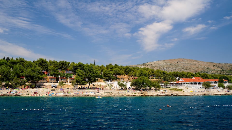 A coastal town with a beach, clear blue sea, and a hill in the background.