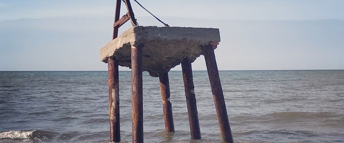 A rusted concrete structure with a pulley system, standing in the ocean waves.