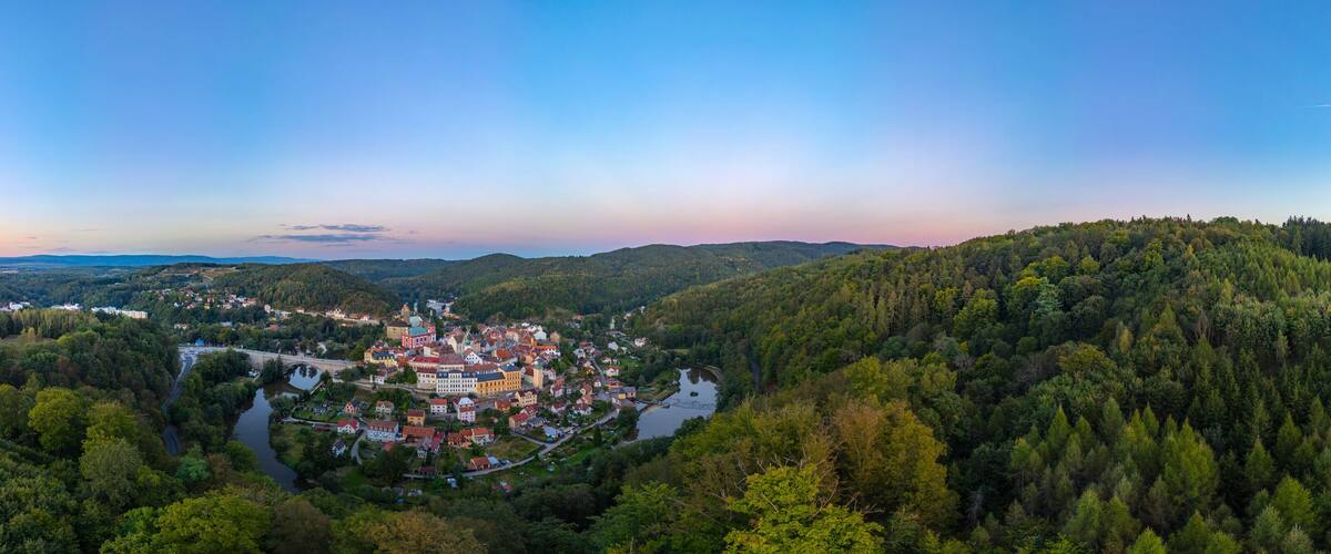 A town nestled in a valley surrounded by dense forests, with a river running through it.