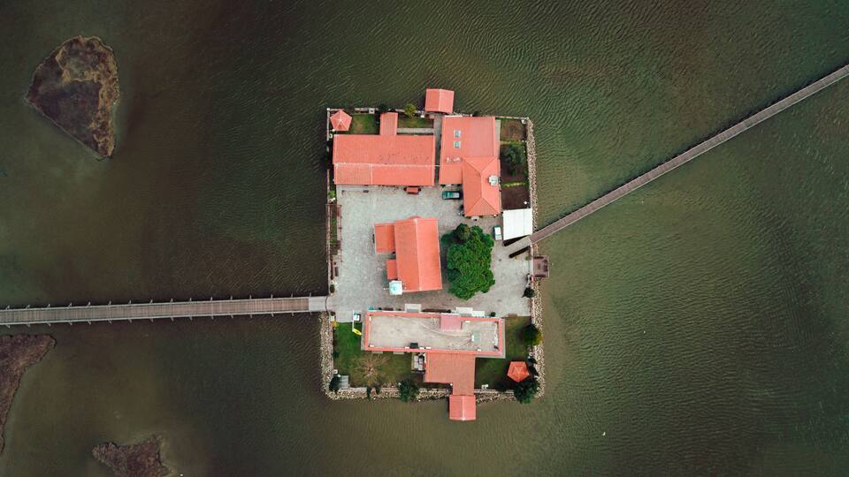 An aerial view of a small island with a red-roofed building, a bridge, and a dock.