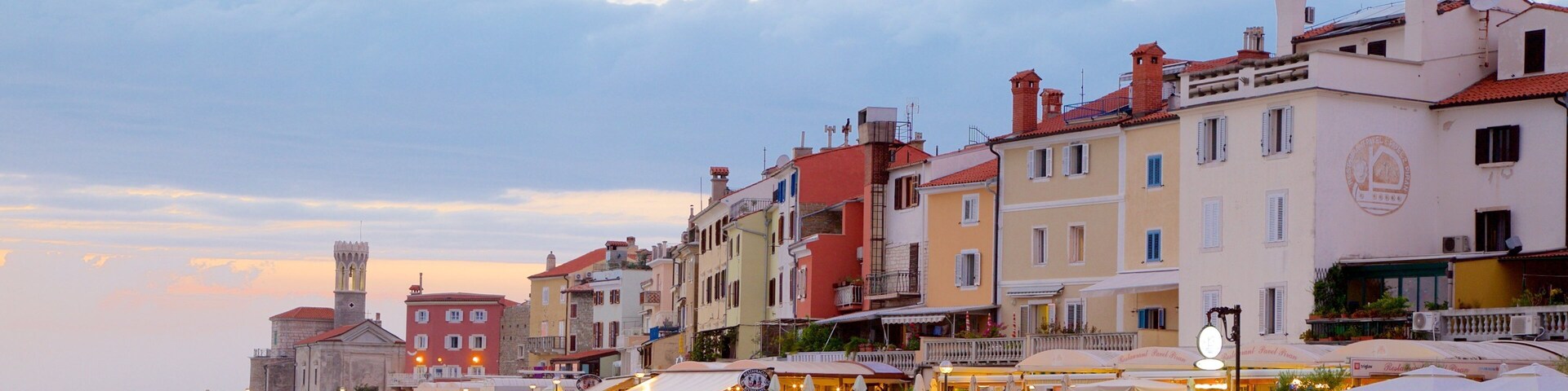 Un pueblo costero con edificios coloridos, una torre histórica y un rompeolas rocoso.