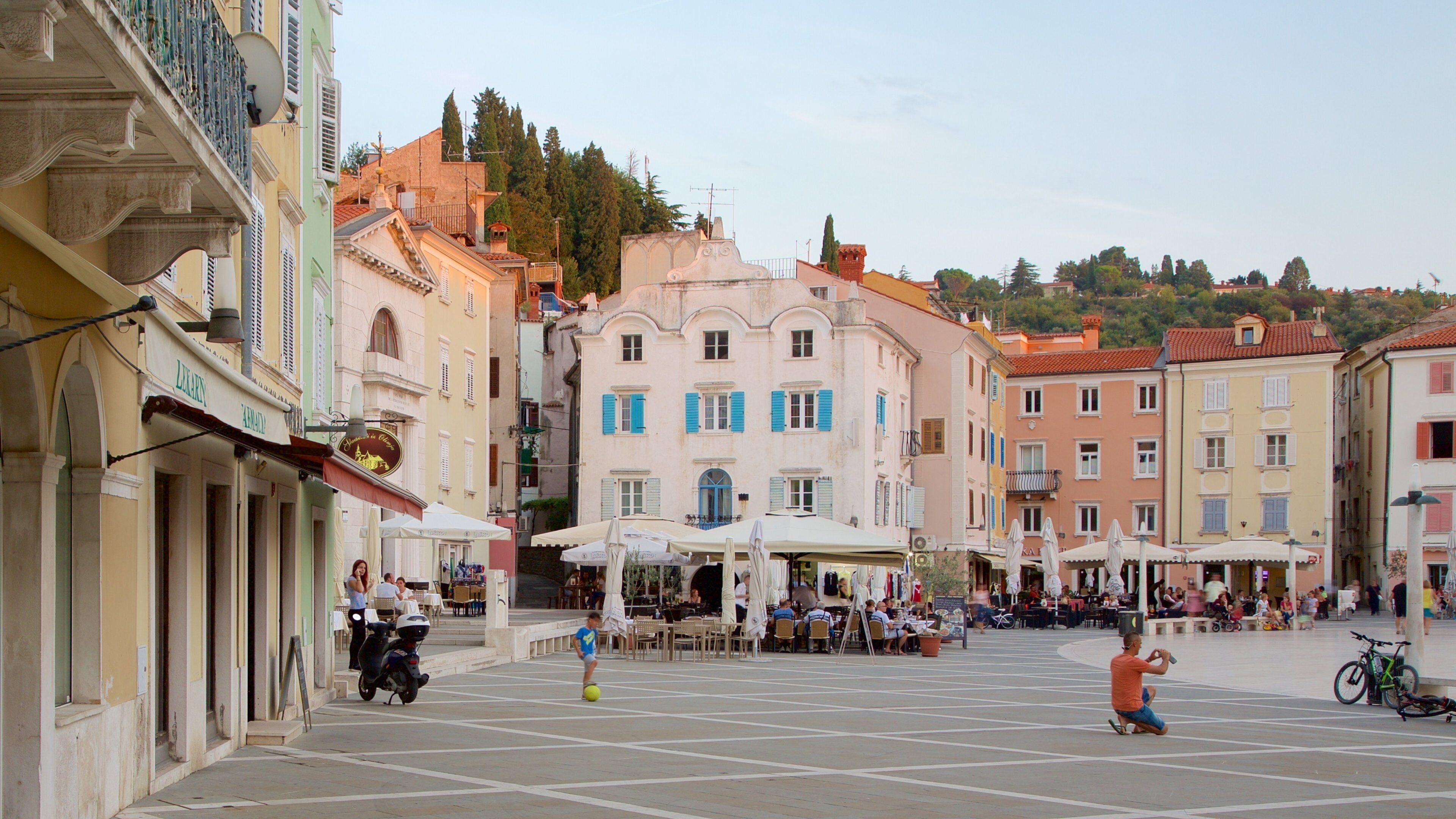 Uma praça com cafés, uma fonte e edifícios históricos.