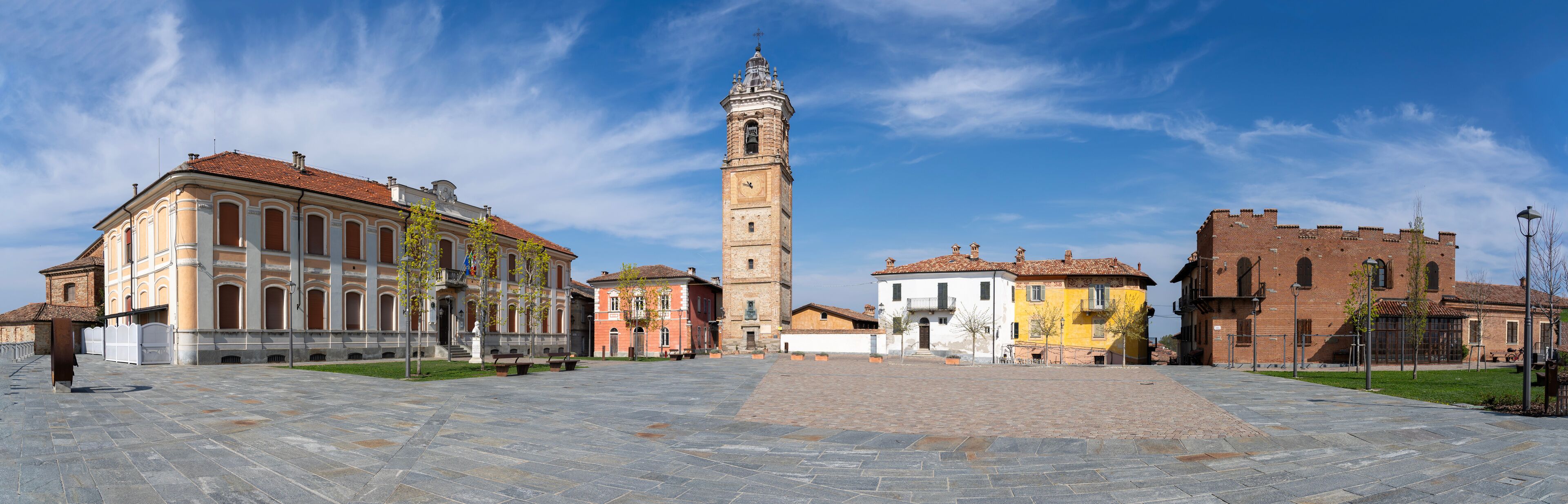 A historic square with a prominent clock tower, surrounded by colorful buildings and a paved plaza.