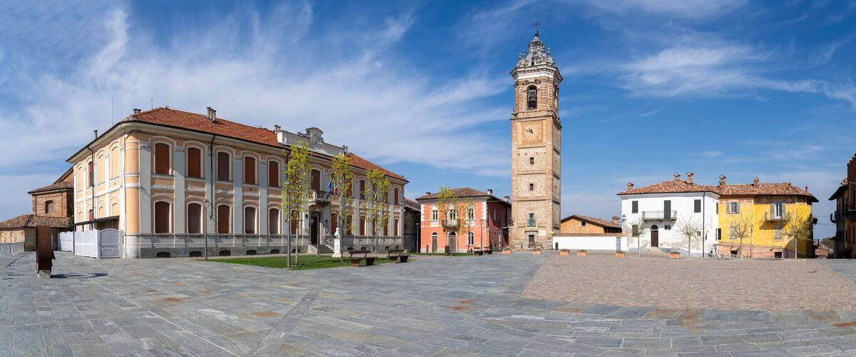 A historic square with a prominent clock tower, surrounded by colorful buildings and a paved plaza.