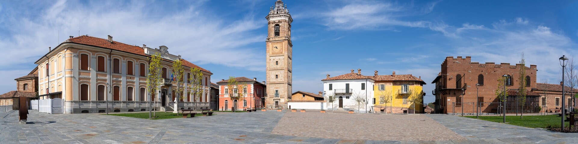A historic square with a prominent clock tower, surrounded by colorful buildings and a paved plaza.