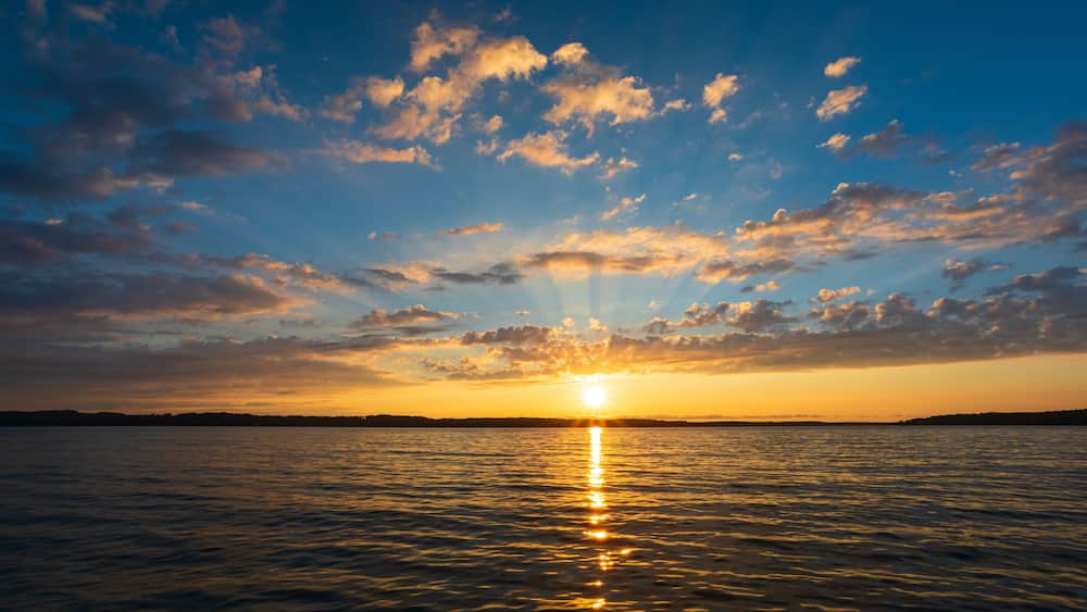 A sunset over a calm sea with a clear horizon and scattered clouds.