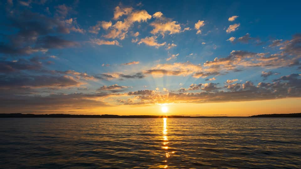 A sunset over a calm sea with a clear horizon and scattered clouds.