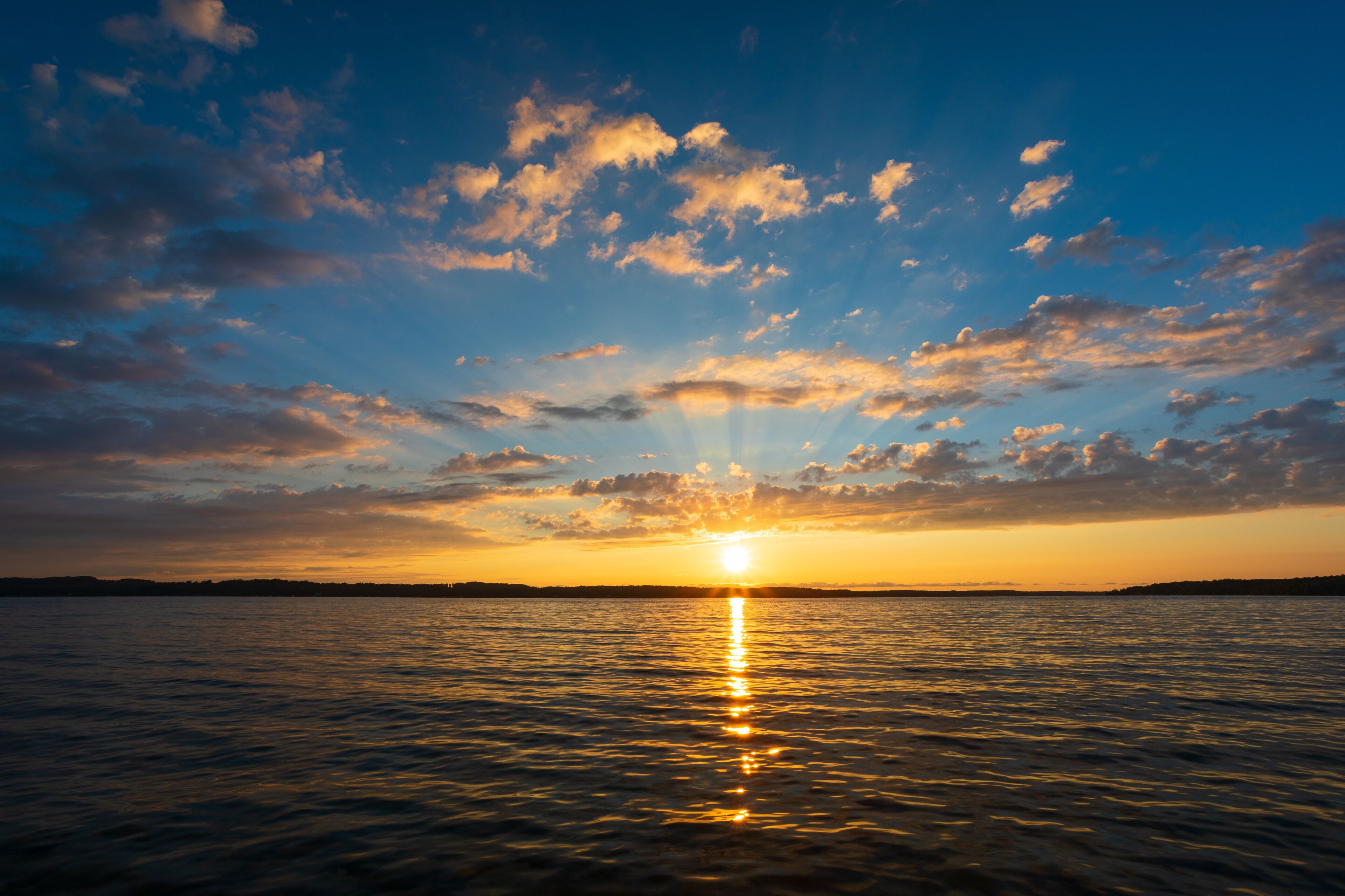 A sunset over a calm sea with a clear horizon and scattered clouds.