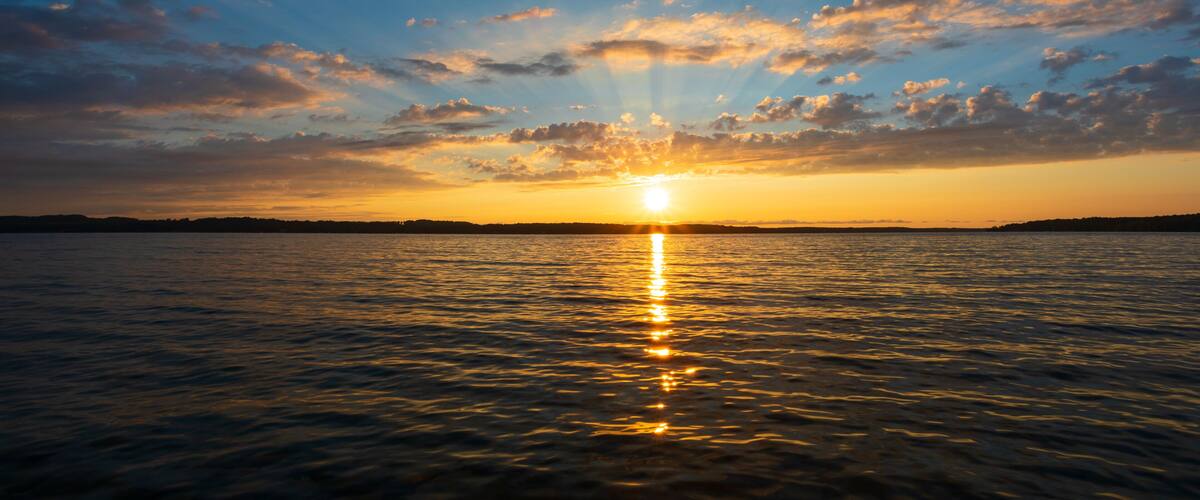 A sunset over a calm sea with a clear horizon and scattered clouds.