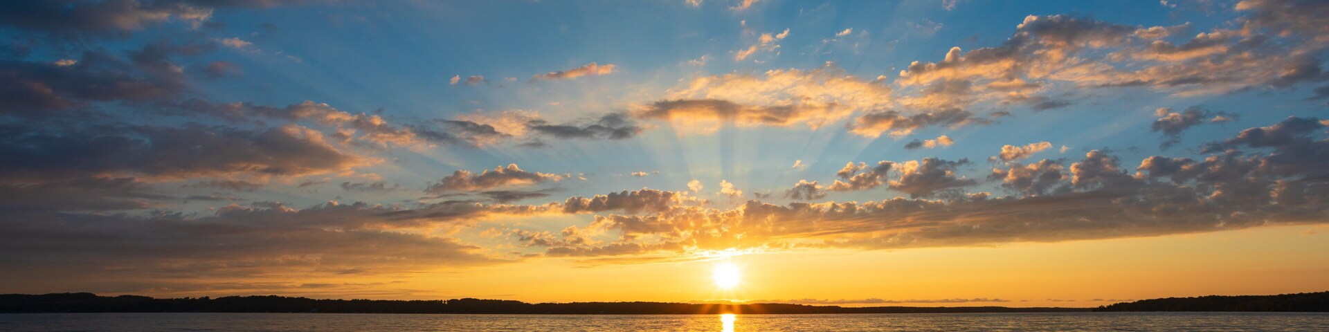 A sunset over a calm sea with a clear horizon and scattered clouds.