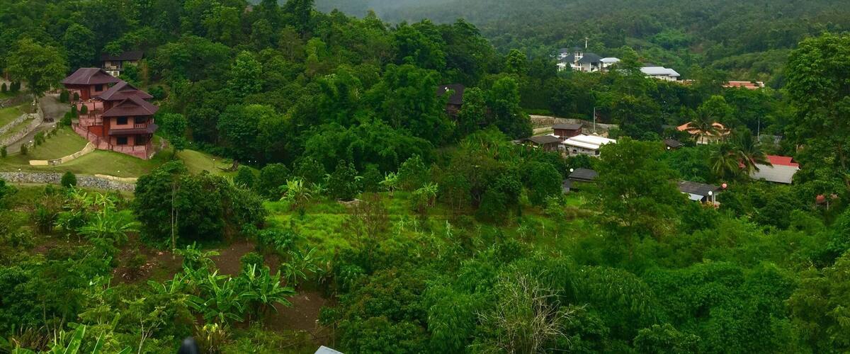 A lush green landscape with a red building and several houses amidst dense forest and mountains.