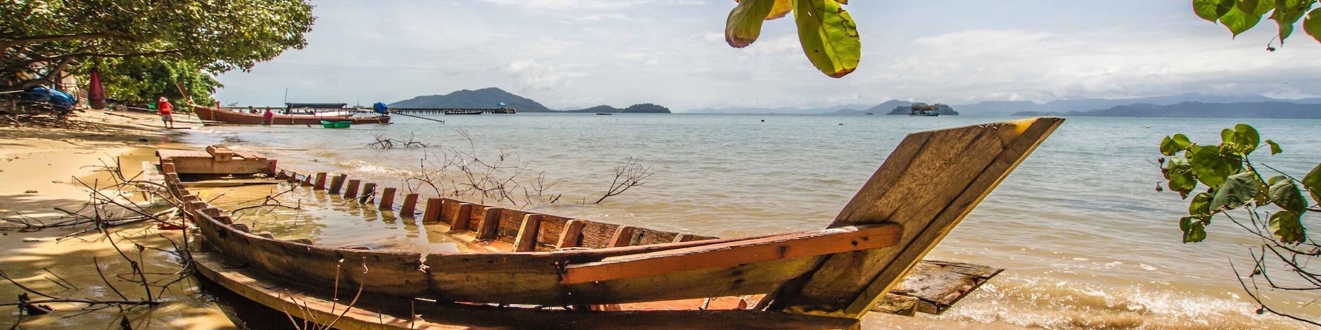 Un bote de madera en una playa arenosa con cielo despejado y islas a lo lejos.
